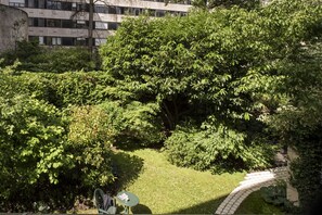 Un jardín exuberante con un sendero pavimentado, una pequeña mesa y una silla.