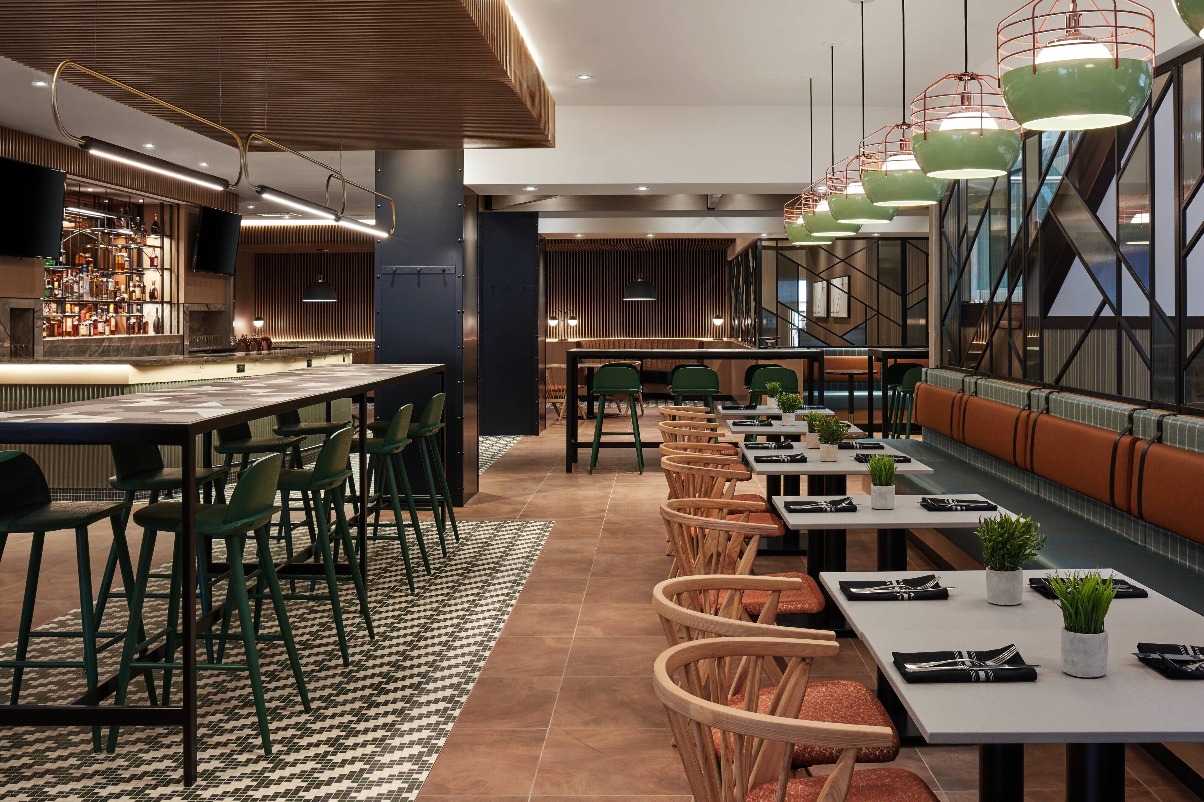 Un restaurante moderno con barra, mesas altas y sillas verdes.