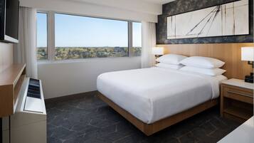 Habitación de hotel con una cama grande, un televisor de pantalla plana, un escritorio, una ventana con vistas a la ciudad y una obra de arte moderna en la pared.