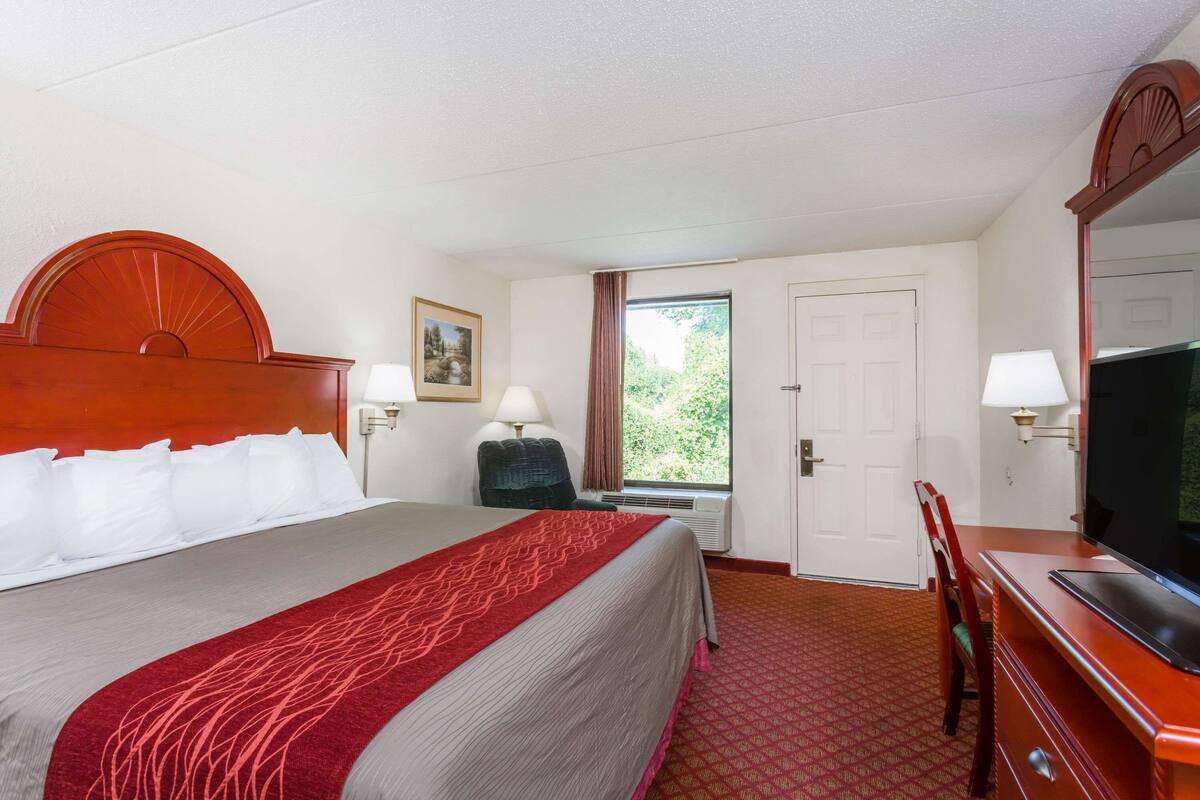 A hotel room with a large bed, a TV, a desk, and a window with curtains.