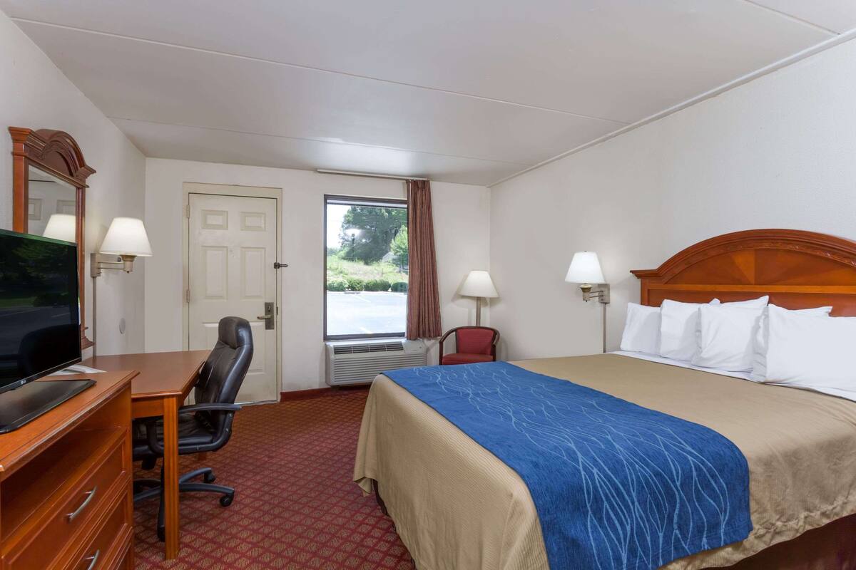 A hotel room with a bed, desk, chair, television, and a window with curtains.