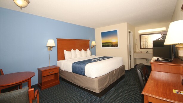 A hotel room with a bed, bedside table, lamp, desk, chair, and a painting on the wall. - Days Inn by Wyndham Winston Salem North (Winston-Salem)