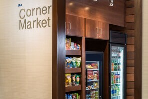 Uma mercearia de esquina com prateleiras repletas de lanches e uma área refrigerada com bebidas.
