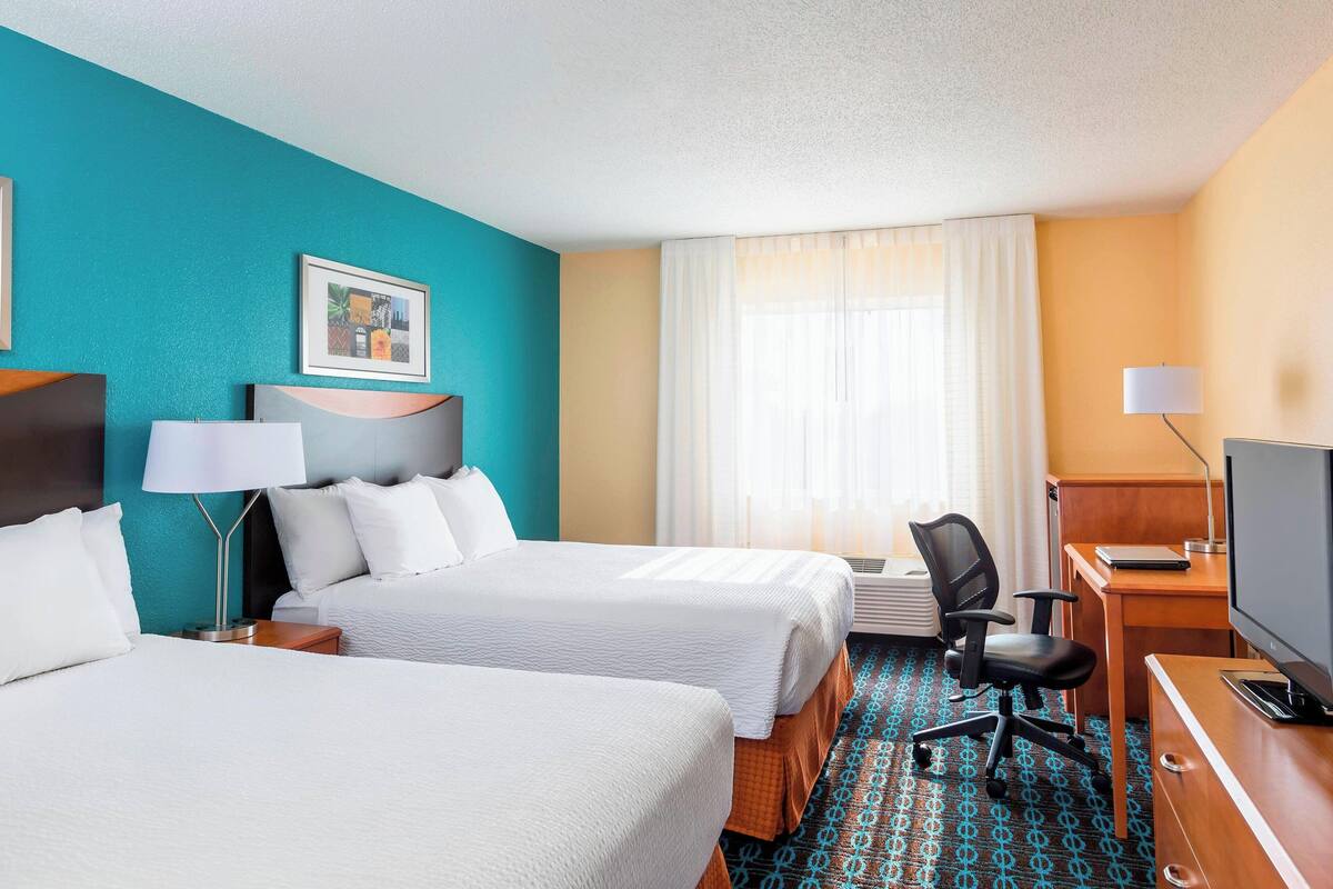 A hotel room with two beds, a desk, a chair, a television, and a window with curtains.