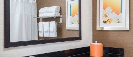 A bathroom with a black countertop, a sink, a mirror, a framed picture, and a towel rack with folded towels.