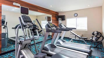 Une salle de sport équipée de tapis de course, d’un mur recouvert de miroirs et d’une horloge.