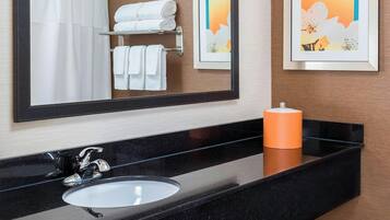 A bathroom with a large mirror, a black countertop, a white sink, and a towel rack with folded towels.