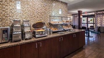 Zona de buffet con distintas estaciones de comida, incluyendo una parrilla caliente, una barra libre y una vitrina con pasteles.