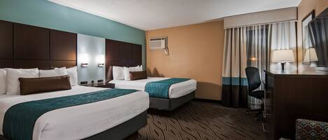 A hotel room with two beds, a desk, a chair, a mirror, and a window with curtains.