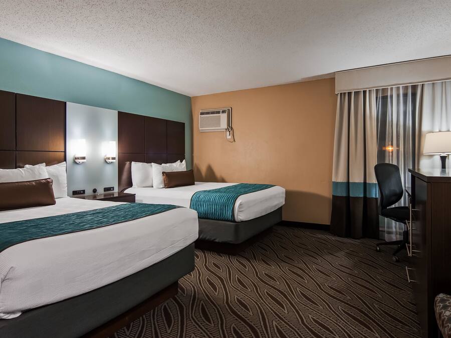 A hotel room with two beds, a desk, a chair, a mirror, and a window with curtains.