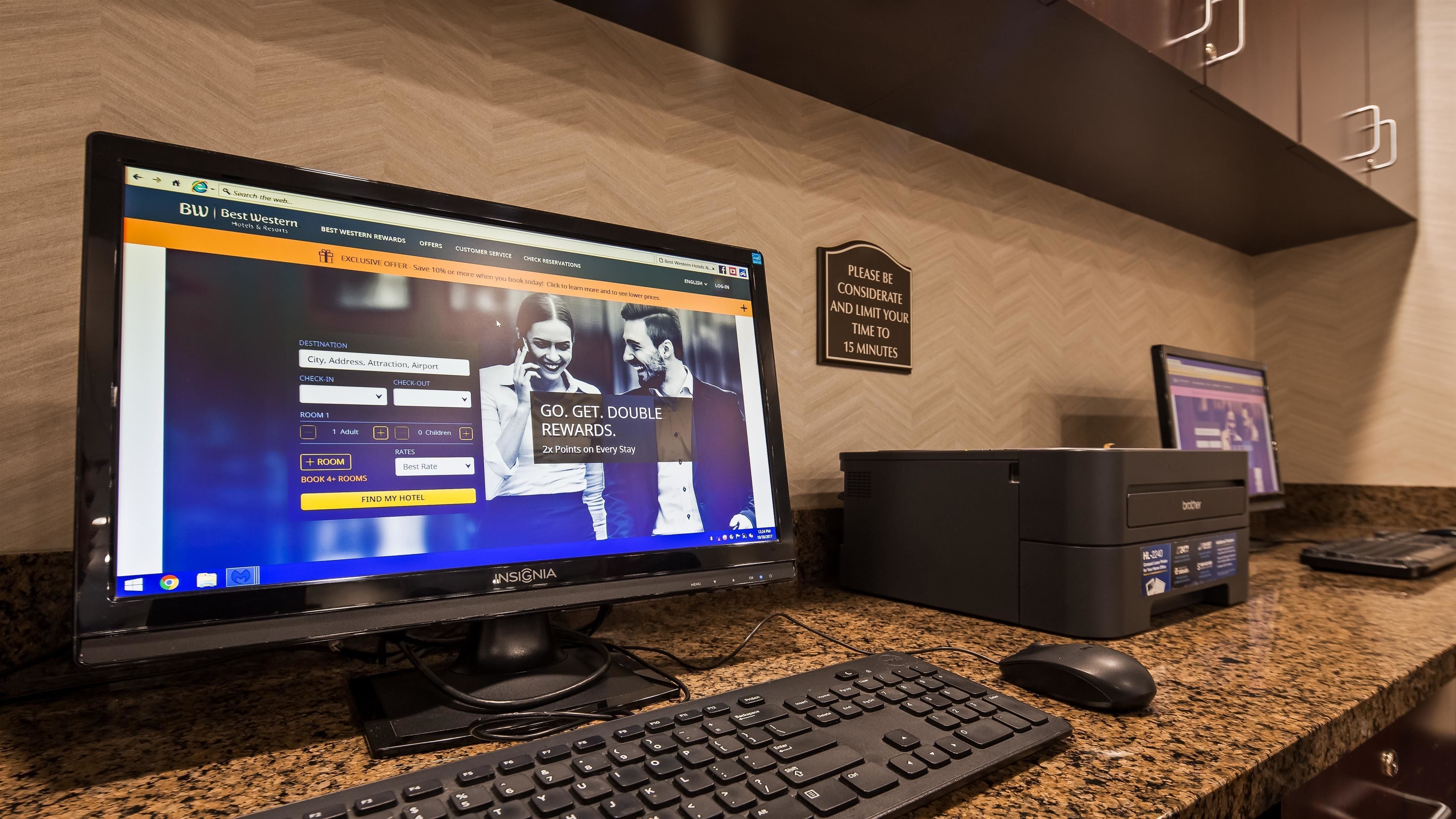 A hotel reception desk with a computer displaying a hotel booking website, a keyboard, a mouse, and a sign on the wall.