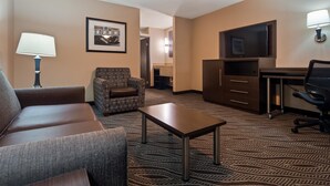 A hotel room with a sofa, armchair, small table, TV, desk, and lamp. - Best Western Plus Galleria Inn & Suites (Memphis)