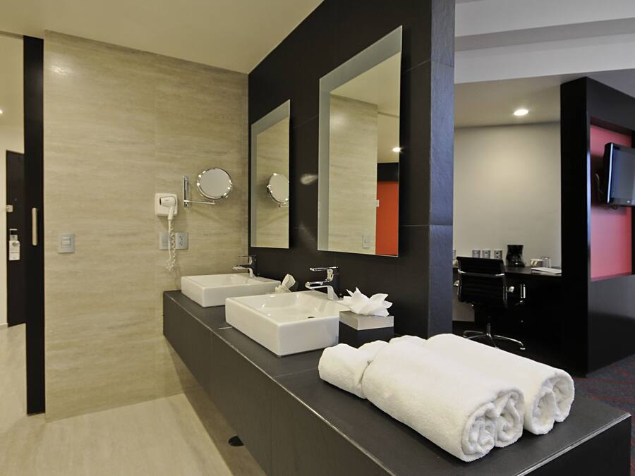 A modern hotel bathroom with two sinks, a large mirror, and a towel rack.
