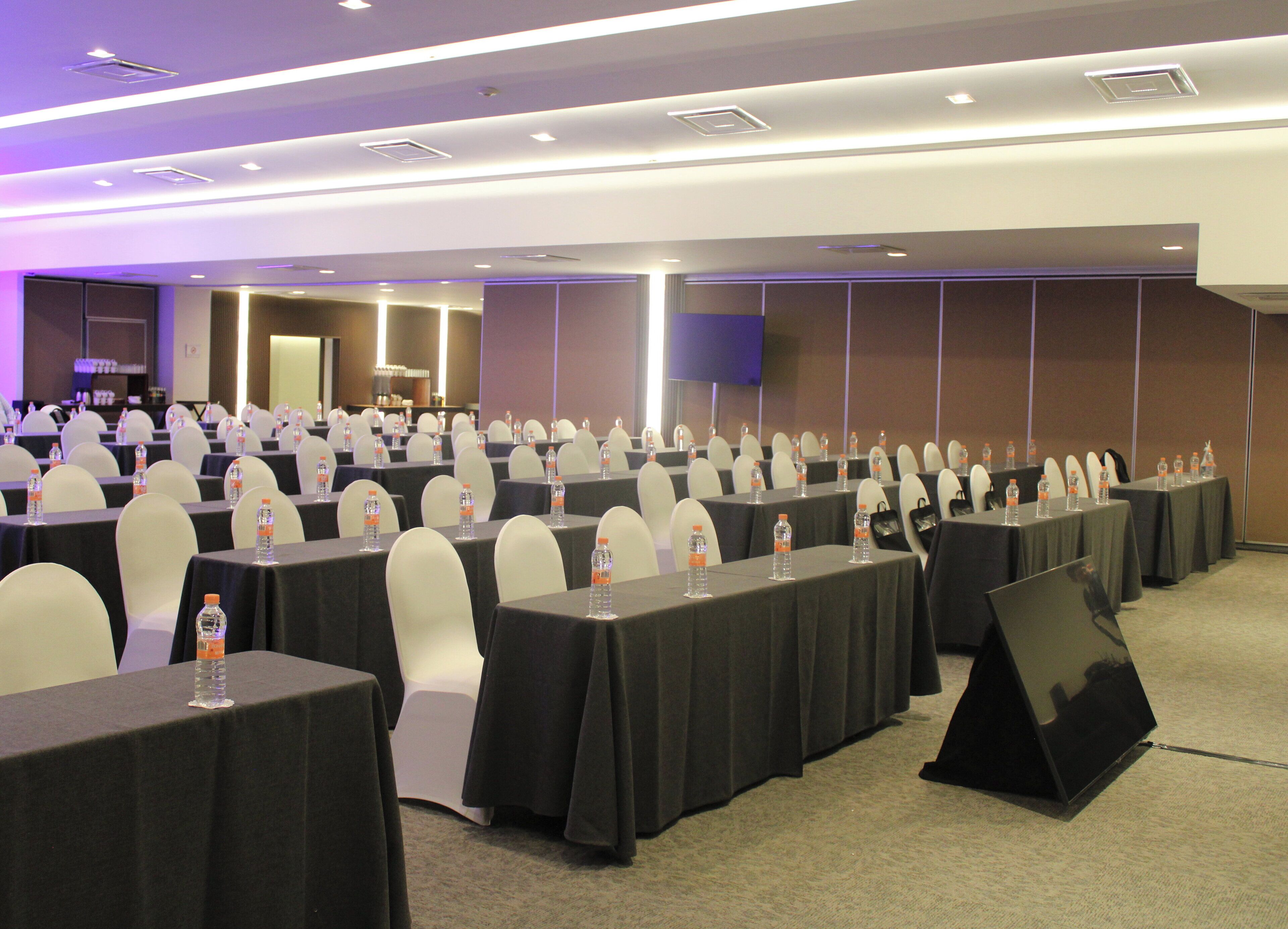 A conference room with rows of tables, chairs, and water bottles.