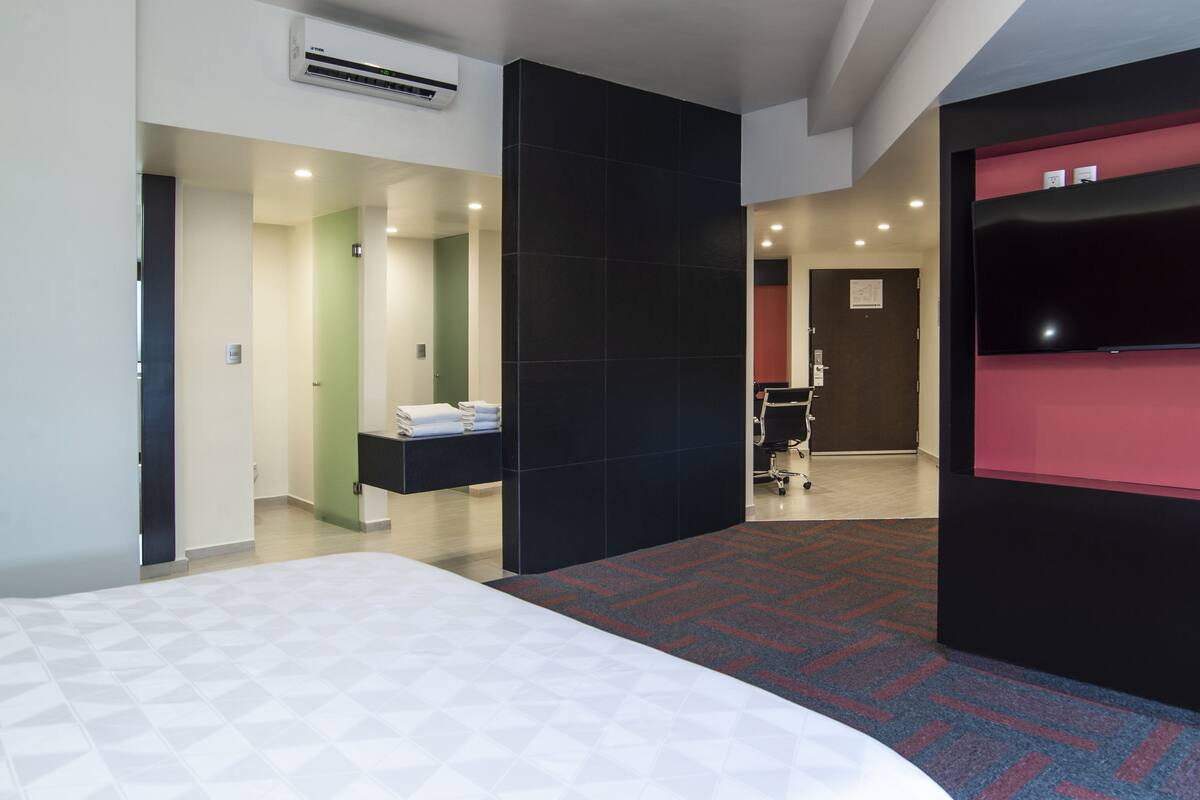 A hotel room with a bed, a desk, a flat-screen TV, and a red accent wall.