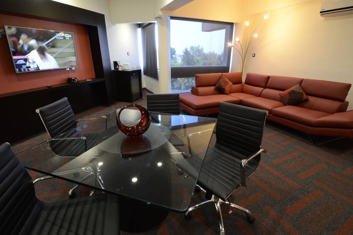 A conference room with a glass table, black chairs, a red sofa, and a TV on the wall.