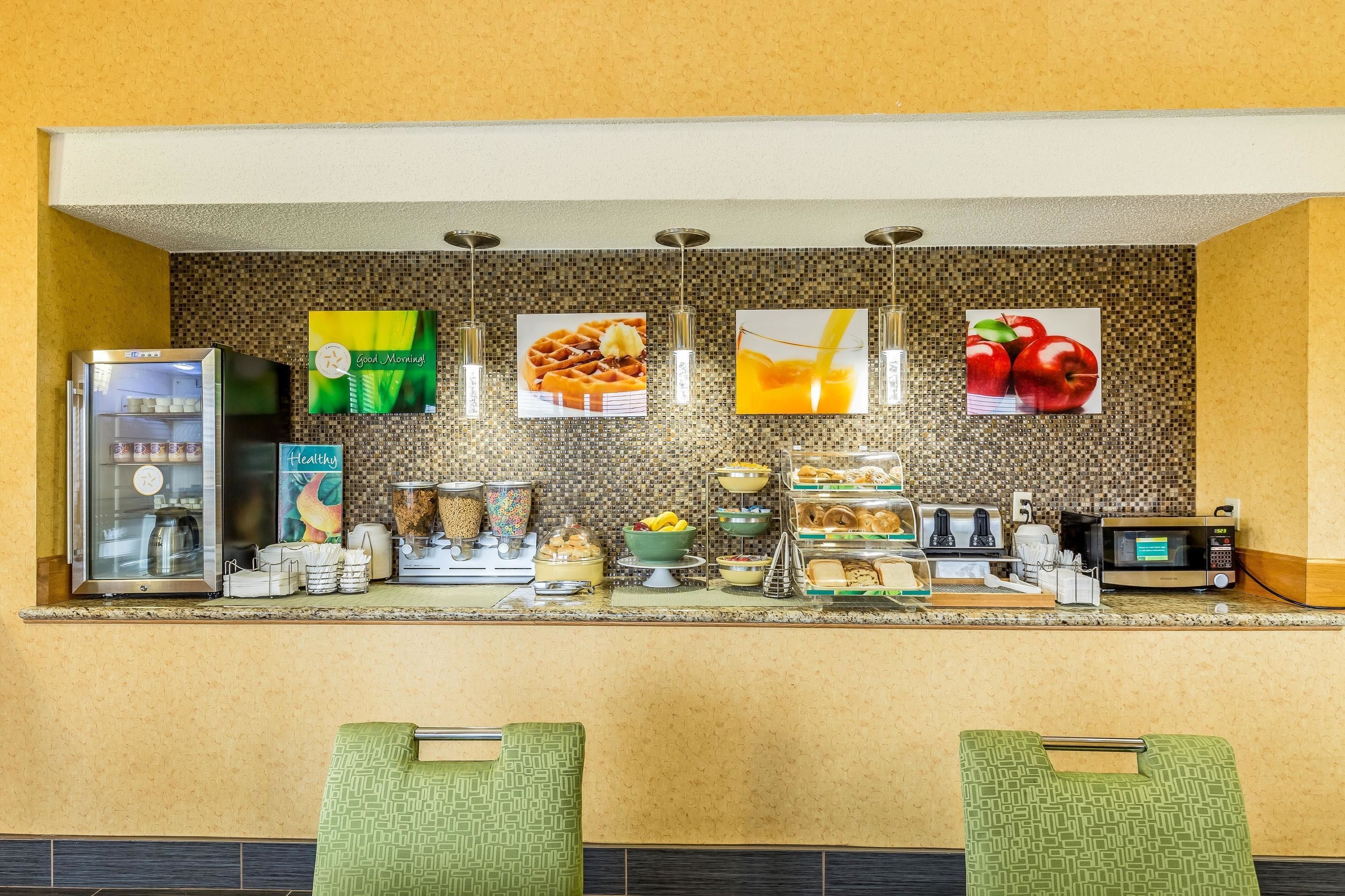 A breakfast bar with a refrigerator, coffee machine, and various food items.