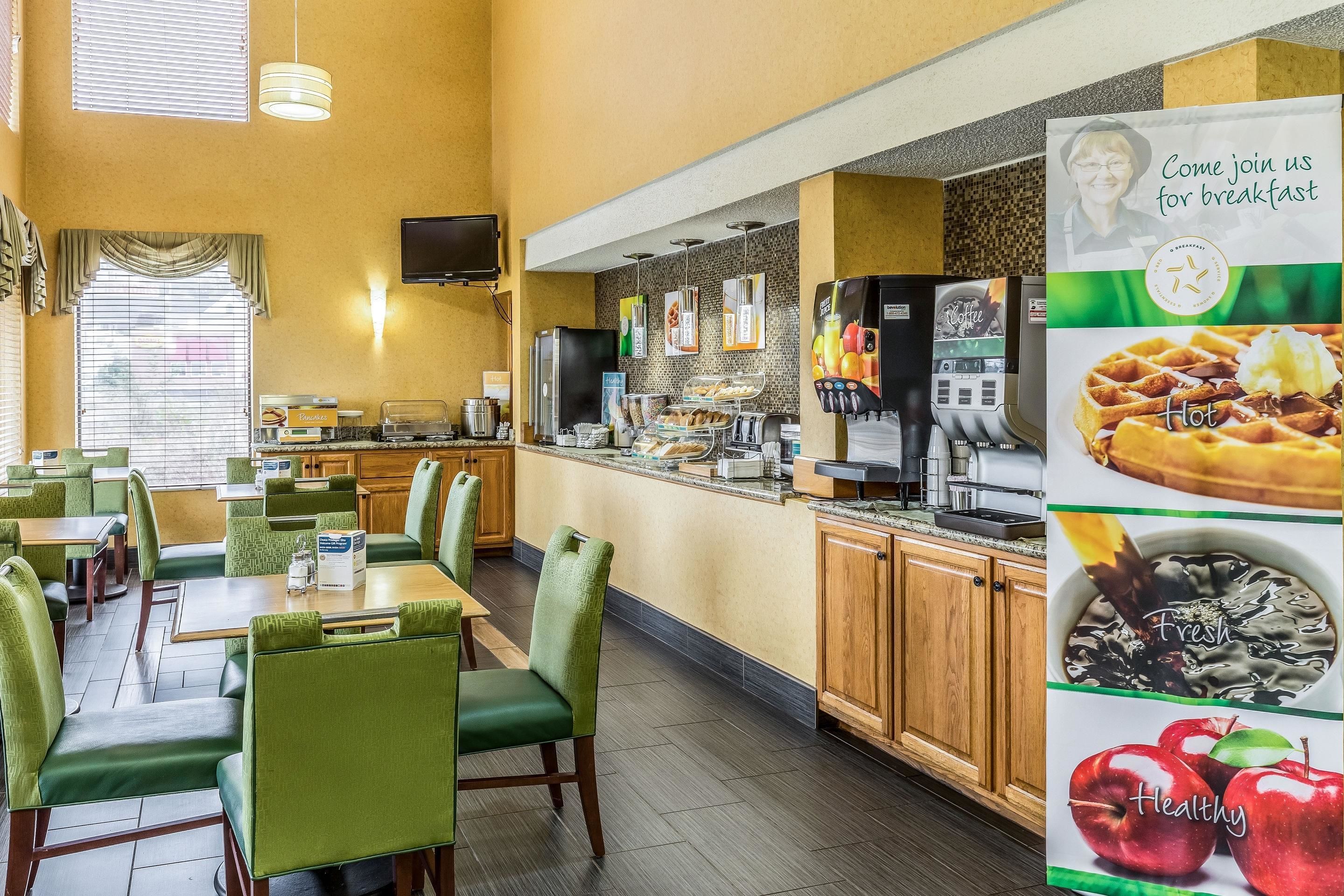 A hotel breakfast area with green upholstered chairs, a buffet counter, and a coffee machine.