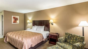 Una habitación de hotel con cama, lámparas de noche, mesita de noche, un sillón estampado con motivos florales y un cuadro en la pared.