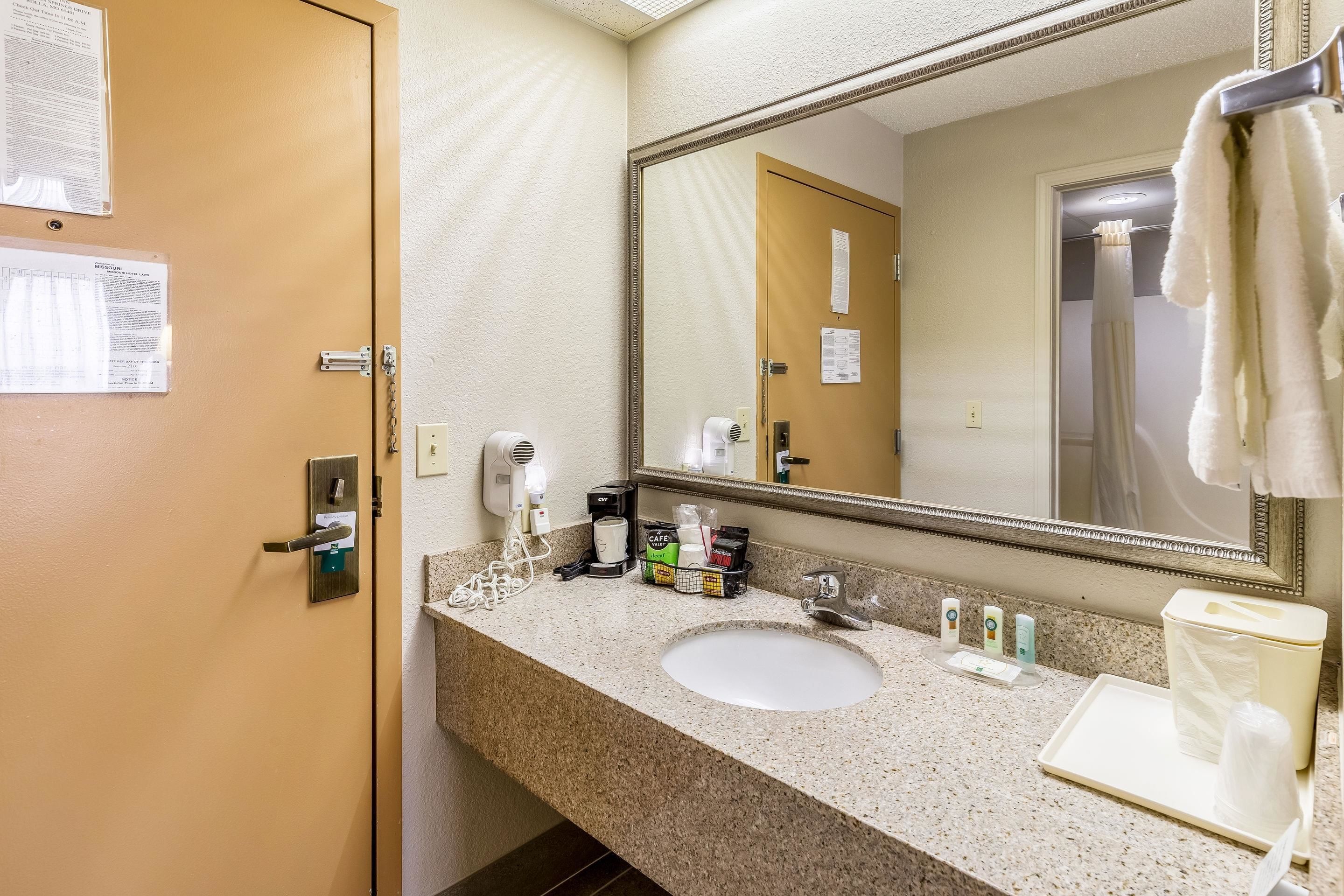 A hotel bathroom with a sink, mirror, towel rack, and toiletries.