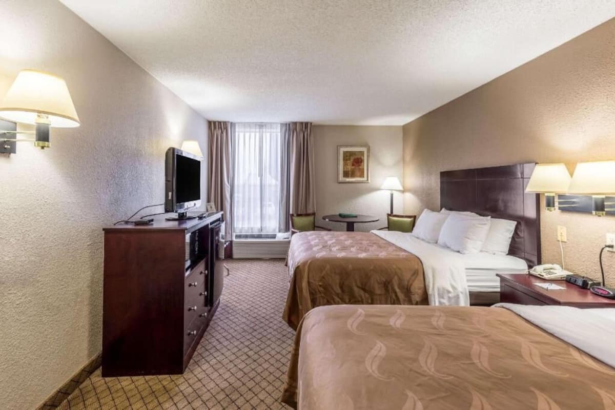 A hotel room with two beds, a desk, a television, and a window with curtains.
