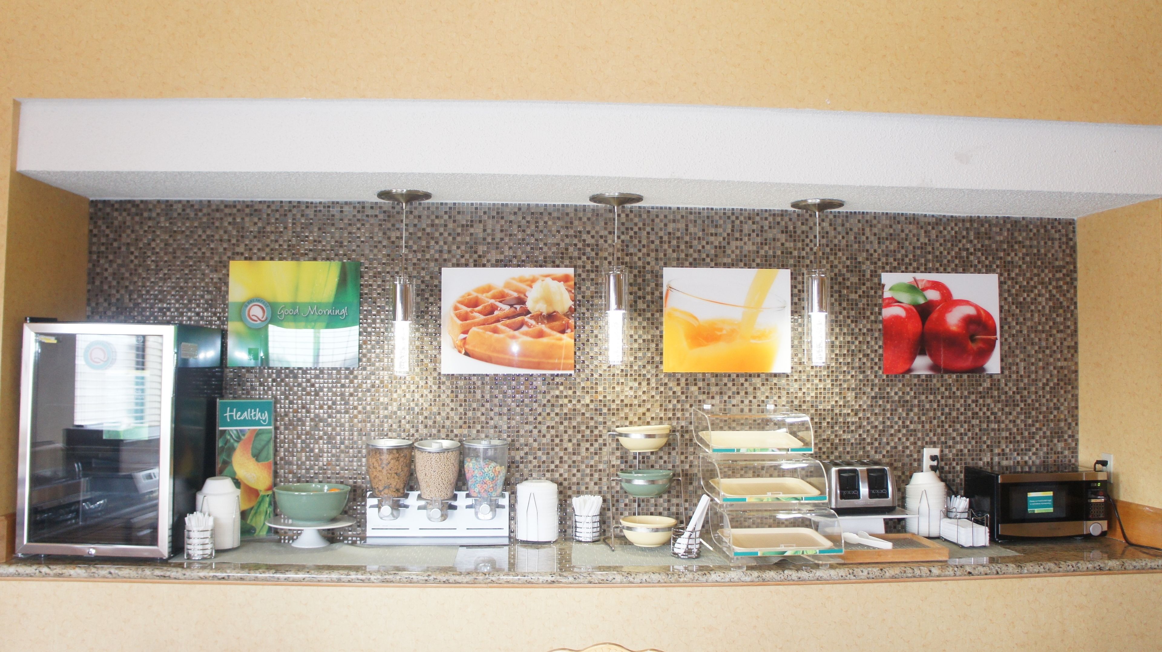 A kitchen with a refrigerator, microwave, toaster, and various kitchen appliances. There are also several framed pictures on the wall.