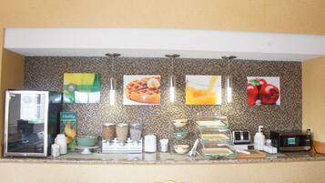 A kitchen with a refrigerator, microwave, toaster, and various kitchen appliances. There are also several framed pictures on the wall.