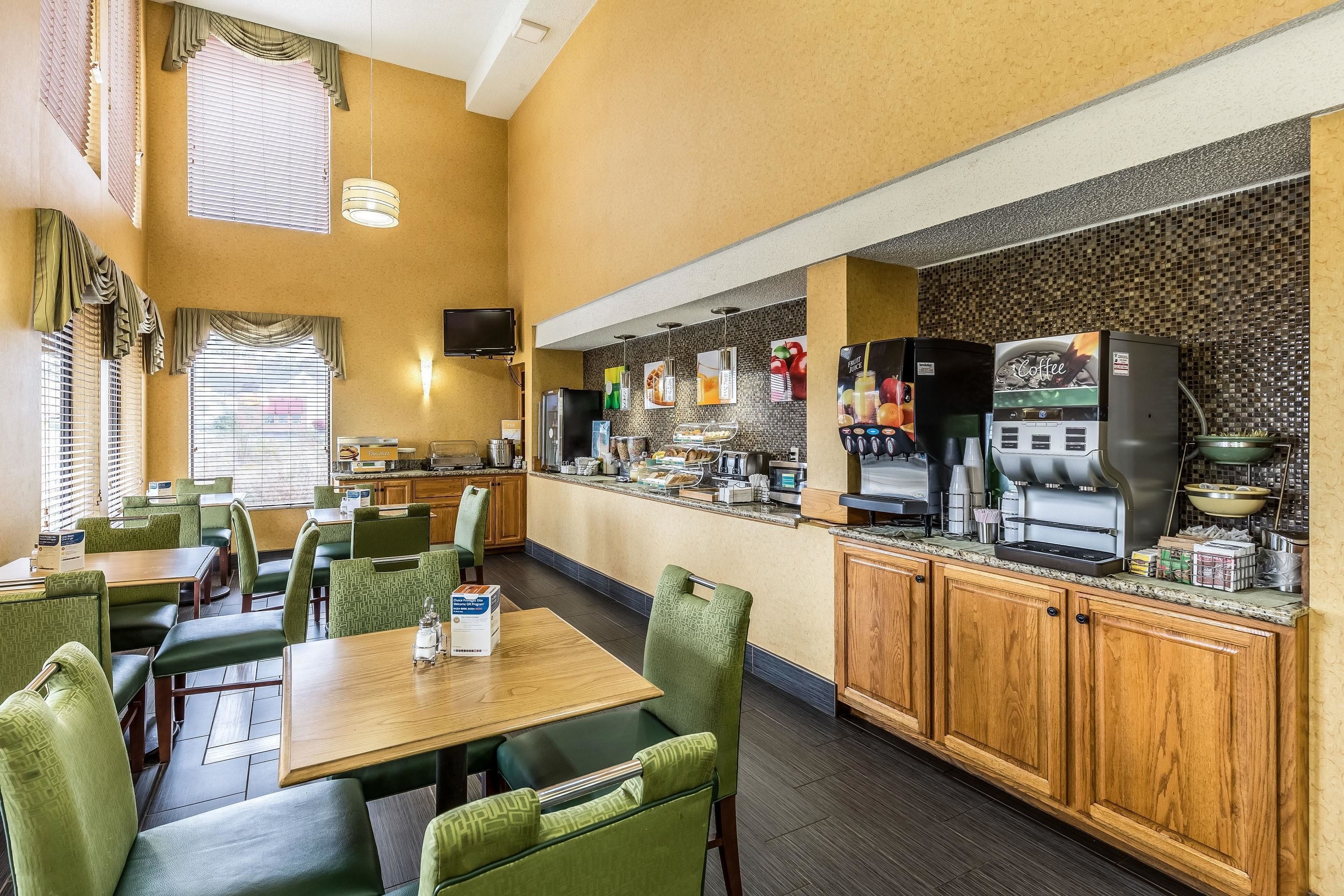 A restaurant with green upholstered chairs, wooden tables, a coffee machine, and a counter with food items.