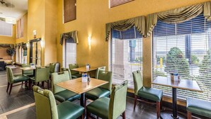 A hotel dining area with green upholstered booths and tables, large windows with blinds, and a view of the outdoors. - Quality Inn Rolla (Rolla)