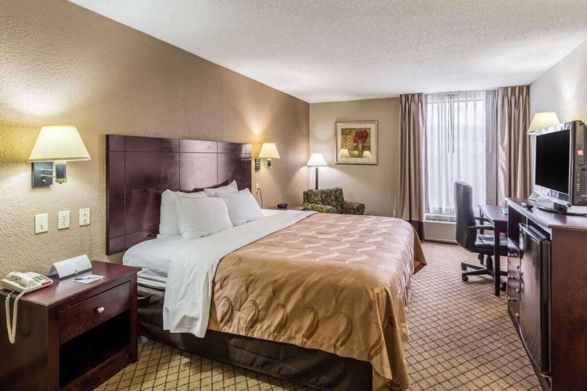 A hotel room with a bed, bedside lamps, a desk with a television, and a chair.