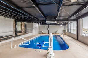 An indoor swimming pool with a diving board, a lifeguard chair, and a pool ladder.