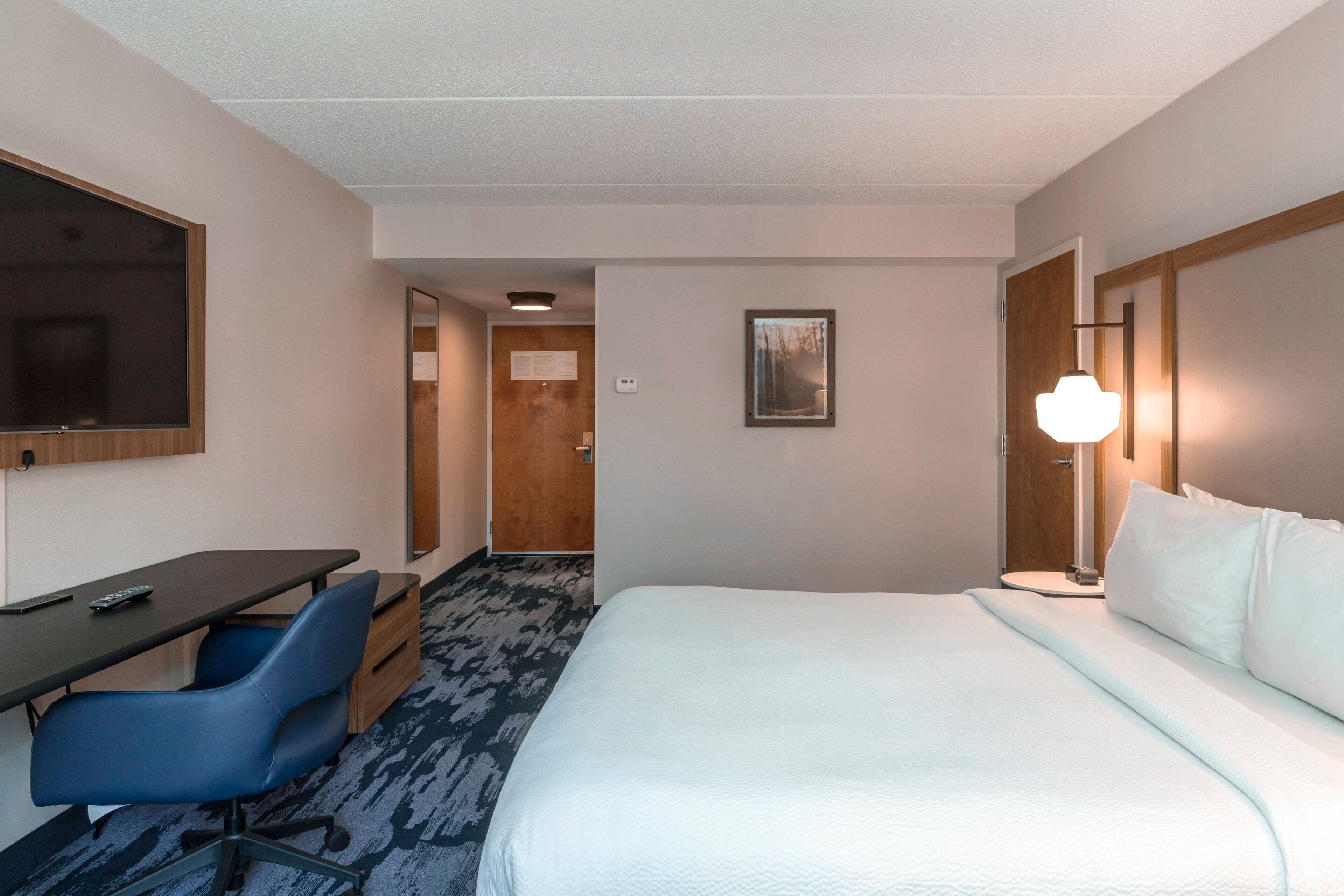 Une chambre d’hôtel comprenant un lit, un bureau, une chaise, une lampe et une porte donnant sur une autre pièce.