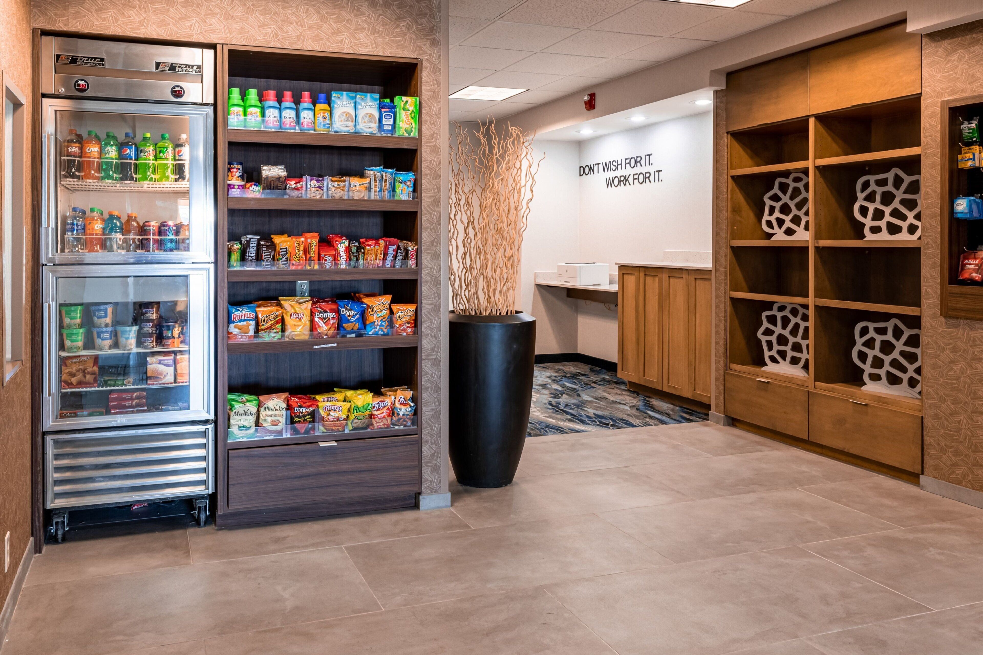 A hotel lobby with a refrigerated beverage display, snack shelves, and a motivational wall quote.