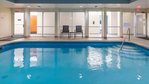 An indoor swimming pool with clear glass walls, two black chairs, and an exit sign.
