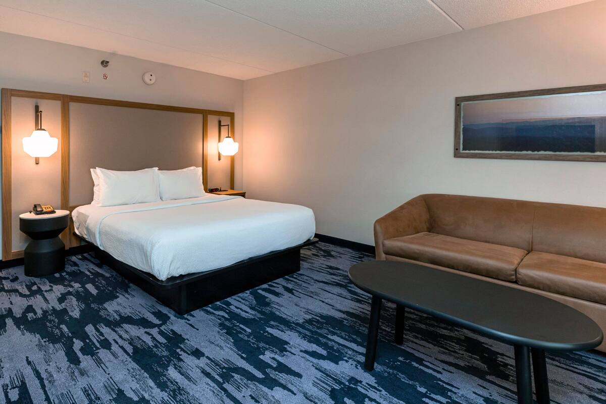Ett hotellrum med en säng, en soffa, ett litet bord och väggmonterade lampor.