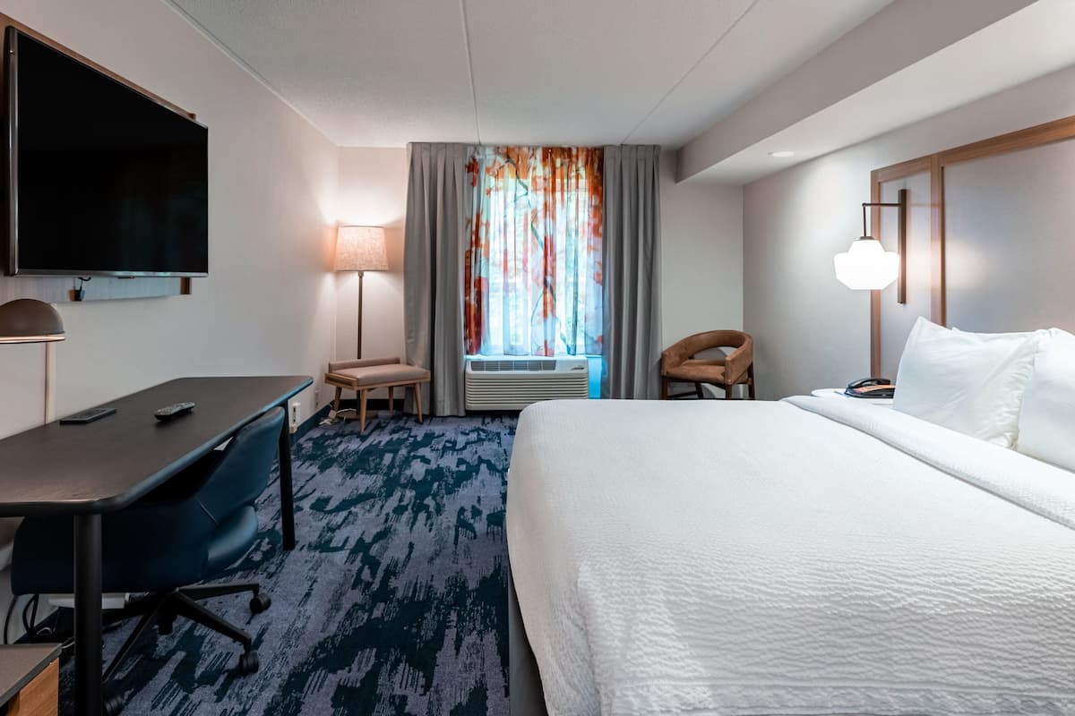 Ett hotellrum med en stor säng, ett skrivbord, en stol, en tv och ett fönster med gardiner.