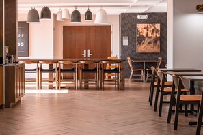 A modern restaurant with wooden tables and chairs, pendant lighting, and a large wooden door in the background. - Fairfield Inn by Marriott Evansville West (Evansville)