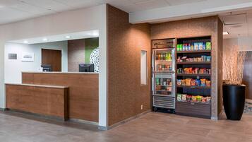 A reception area with a wooden counter, a refrigerator stocked with beverages and snacks, and a large potted plant.