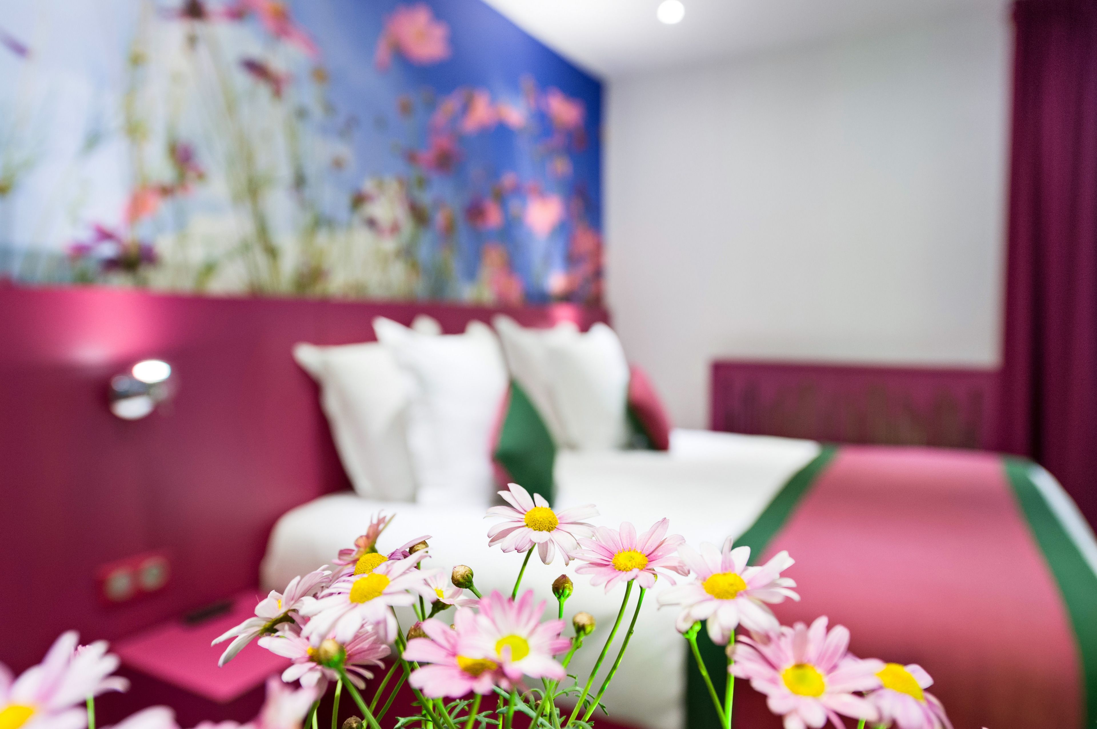 A hotel room with a bed, a nightstand, and a vase of flowers.