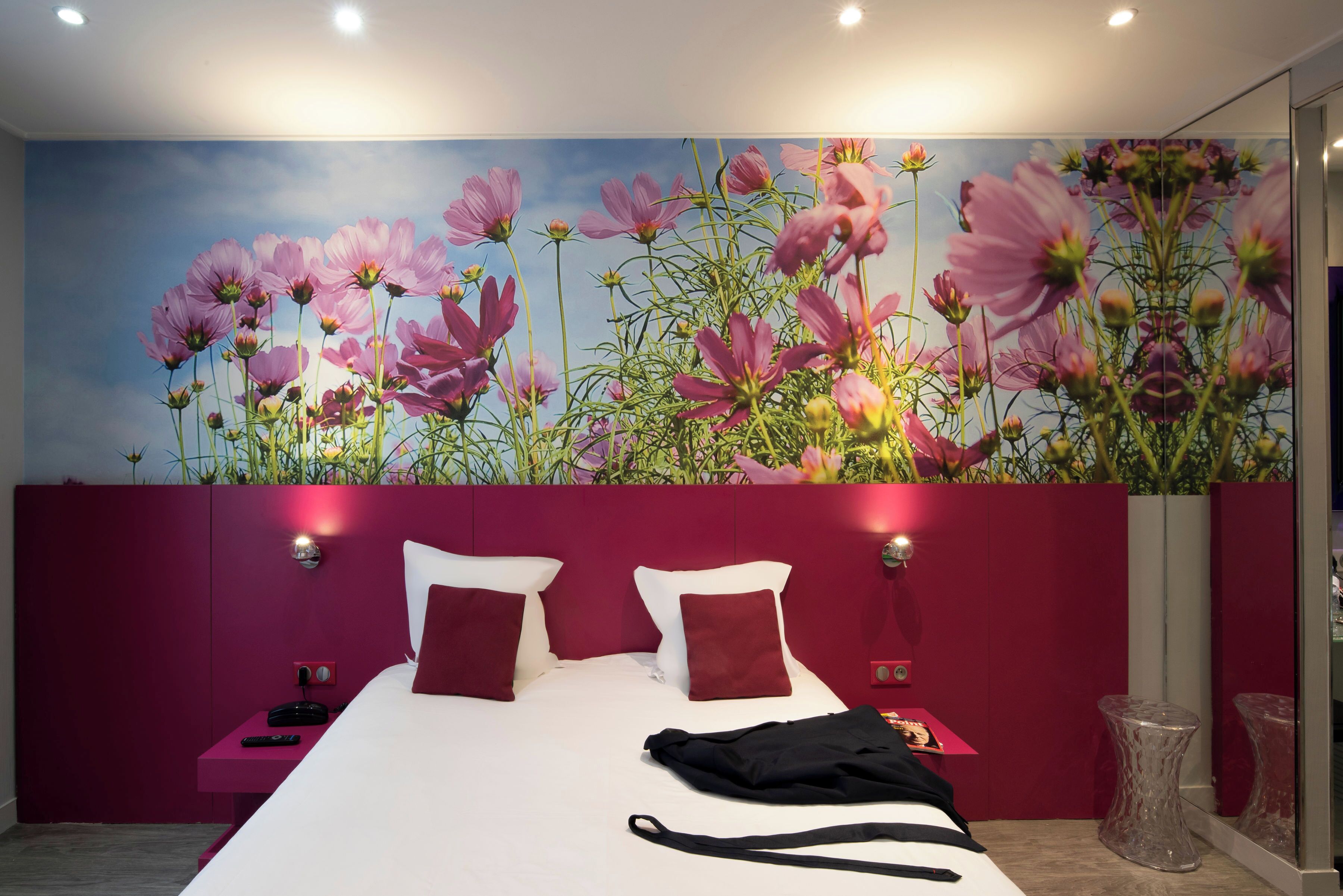 A bedroom with a large bed, red headboard, and a wall mural of pink flowers.