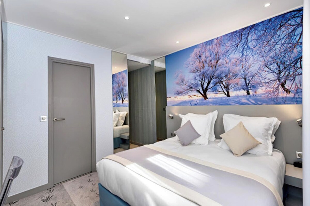 A hotel room with a large bed, a door, and a wall-mounted painting of a snowy landscape.