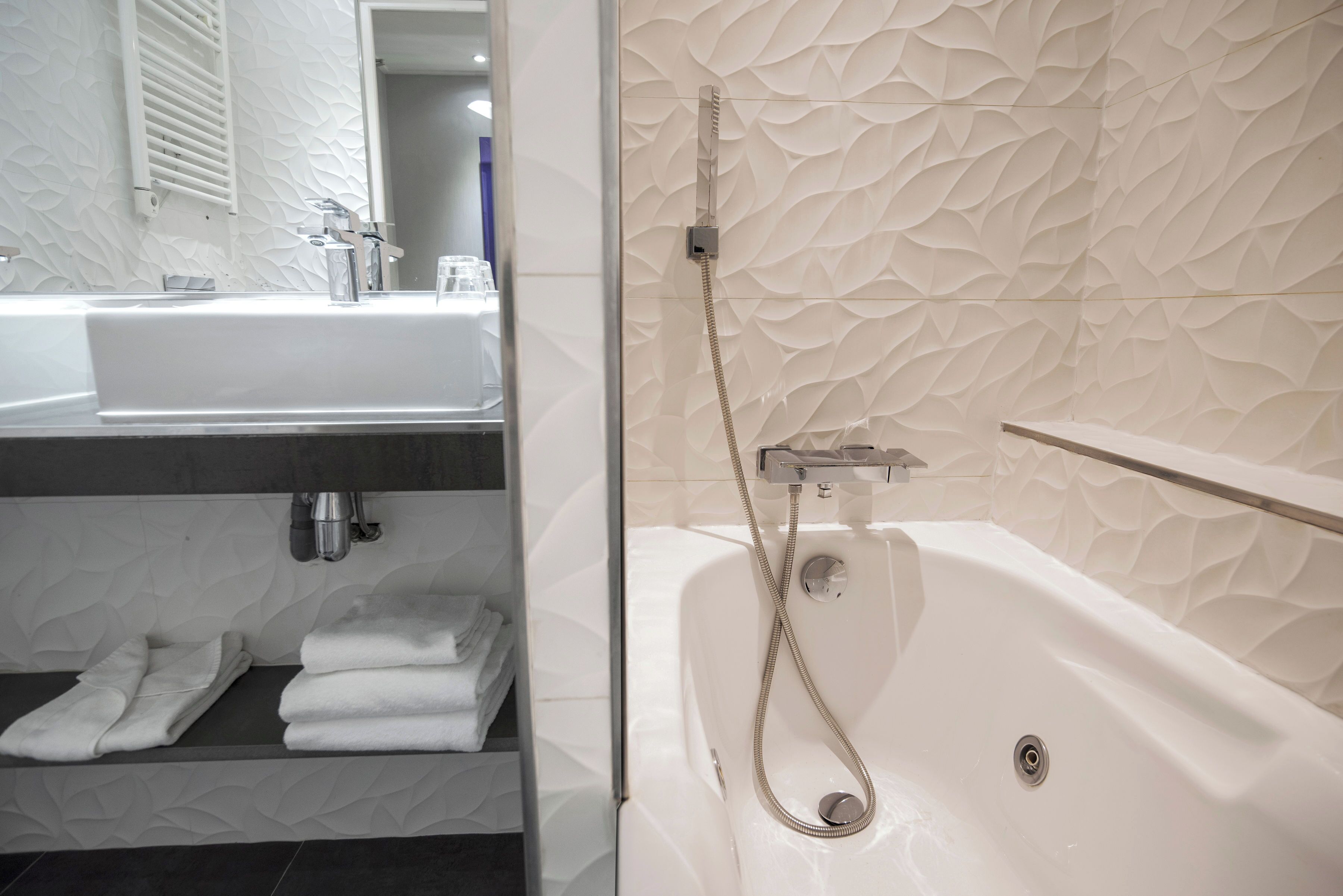A modern bathroom with a white sink, a bathtub, and a towel rack.