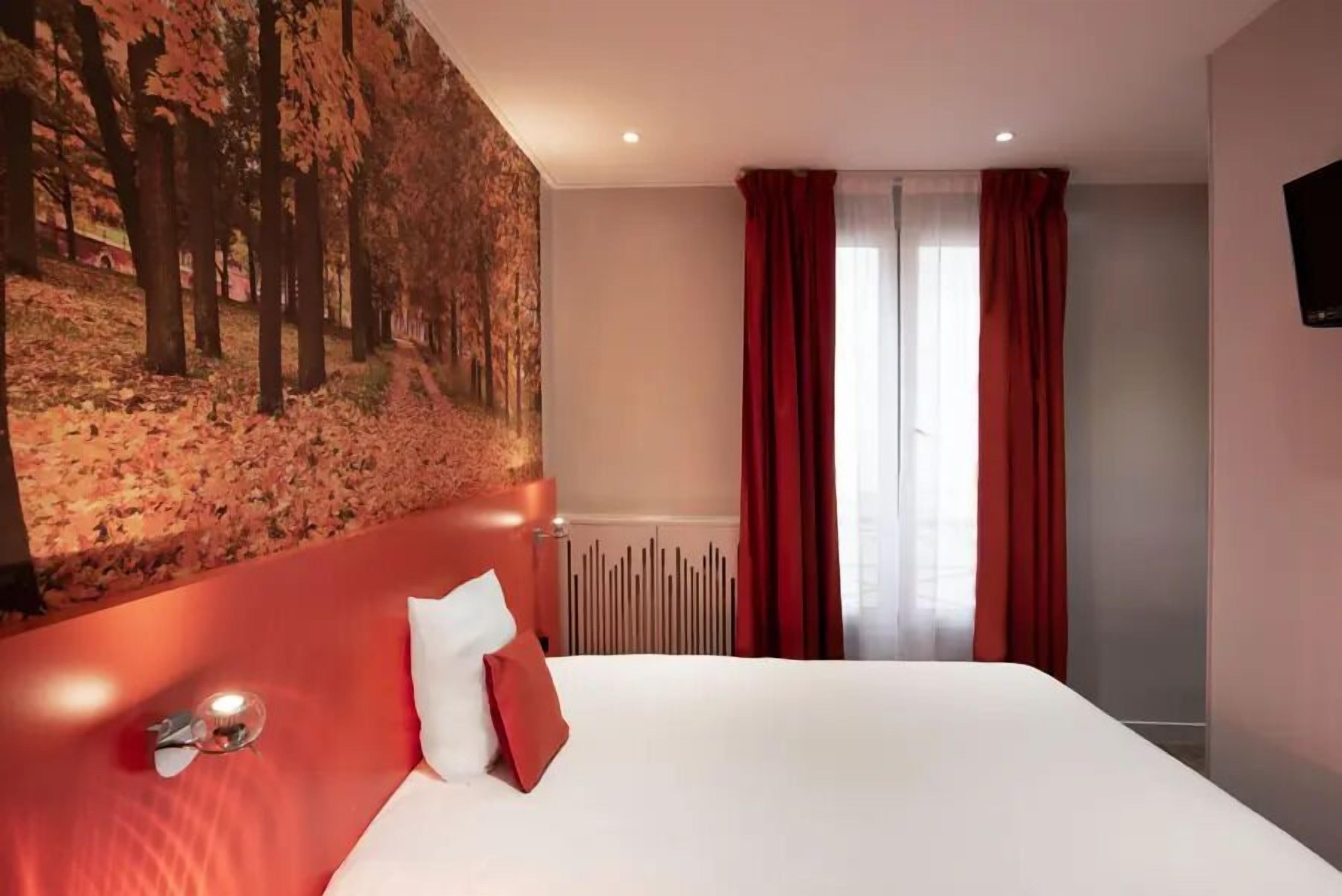 A hotel room with a large bed, a headboard with a forest mural, red curtains, and a radiator.