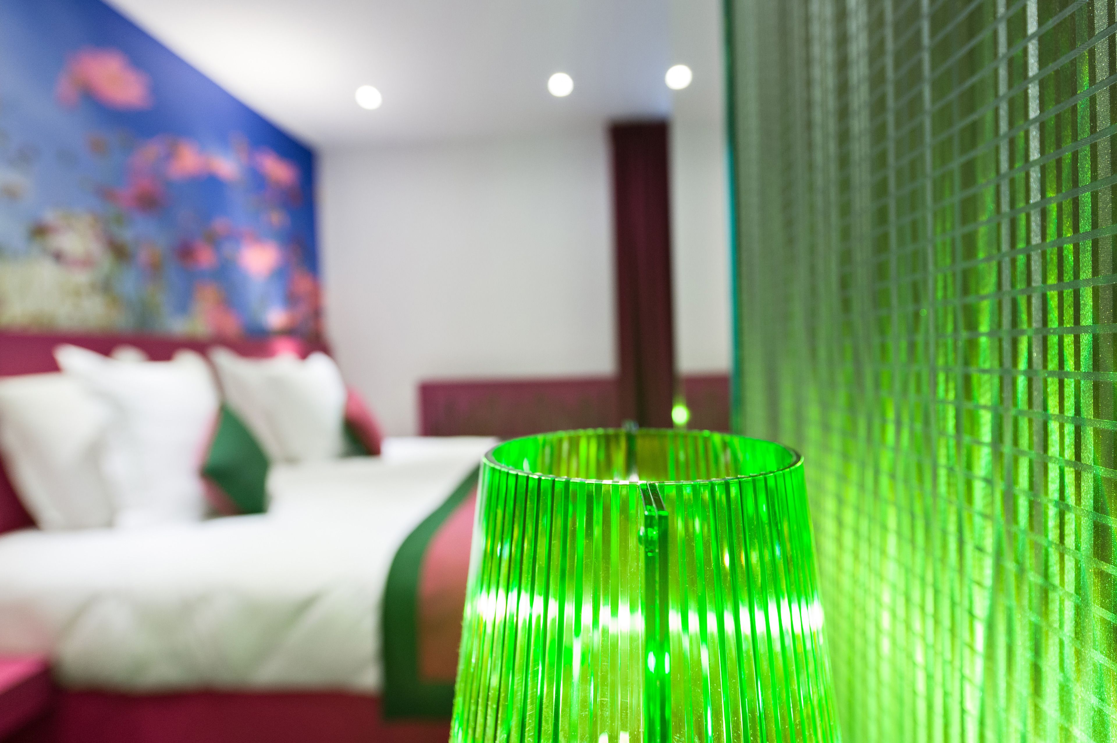 A hotel room with a bed, a green lamp, and a wall with a floral mural.