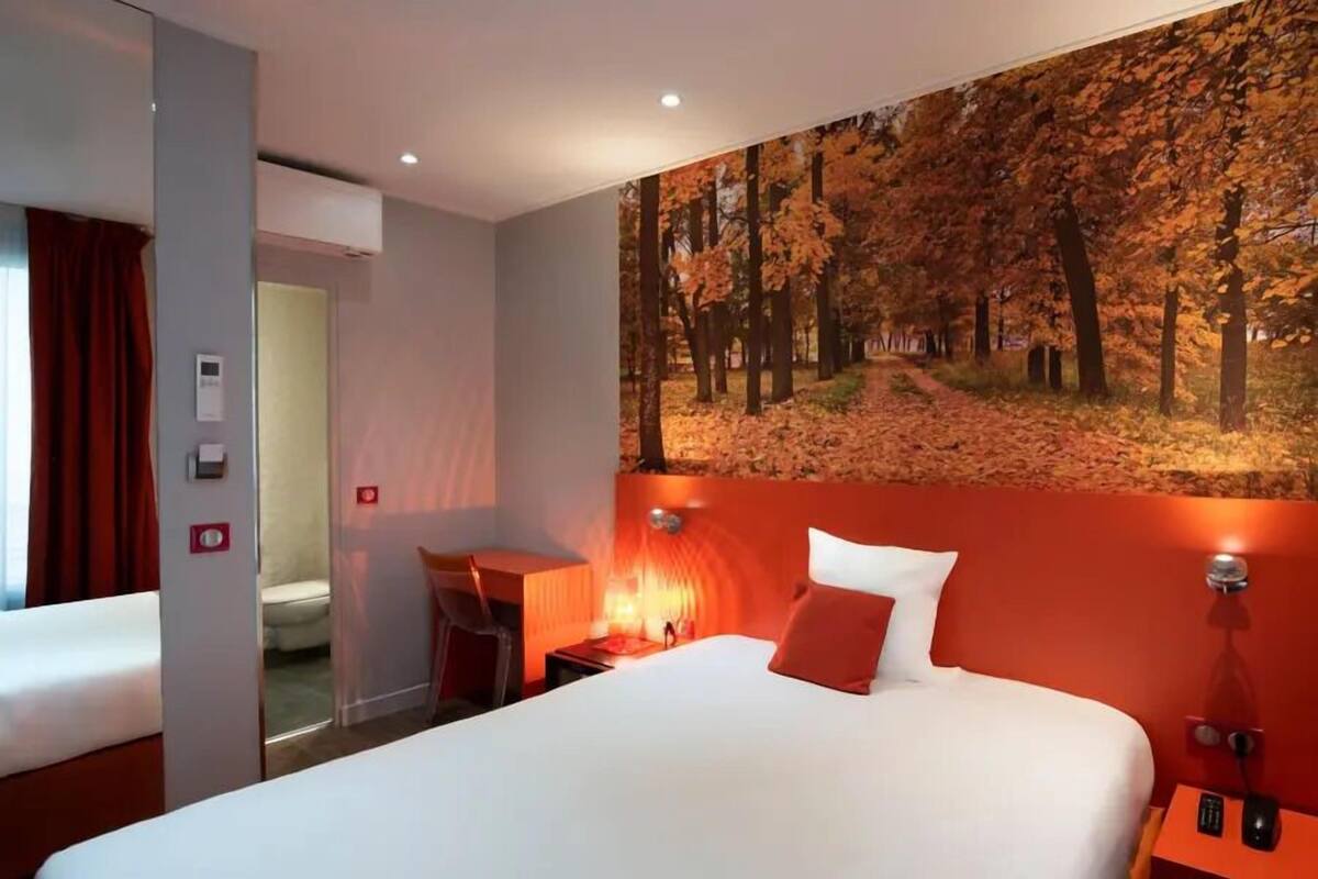 A hotel room with a large bed, a desk, a chair, and a painting of a forest on the wall.