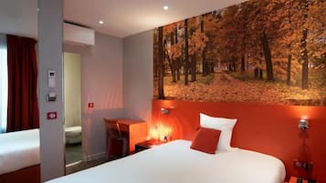 A hotel room with a large bed, a desk, a chair, and a painting of a forest on the wall.