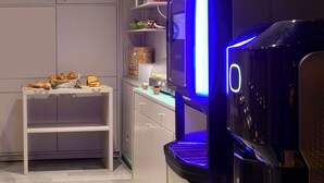 A kitchen area with a modern coffee machine, a white table with food items, and a shelf with kitchenware. - Hotel Les Jardins de Montmartre (Paris)