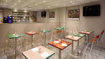 Un restaurante moderno con mesas y sillas de vidrio transparente, una barra con una máquina de café y obras de arte en las paredes.