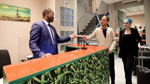 A reception desk with a glass partition, a staircase in the background, and a painting of the Eiffel Tower. - Hotel Les Jardins de Montmartre (Paris)