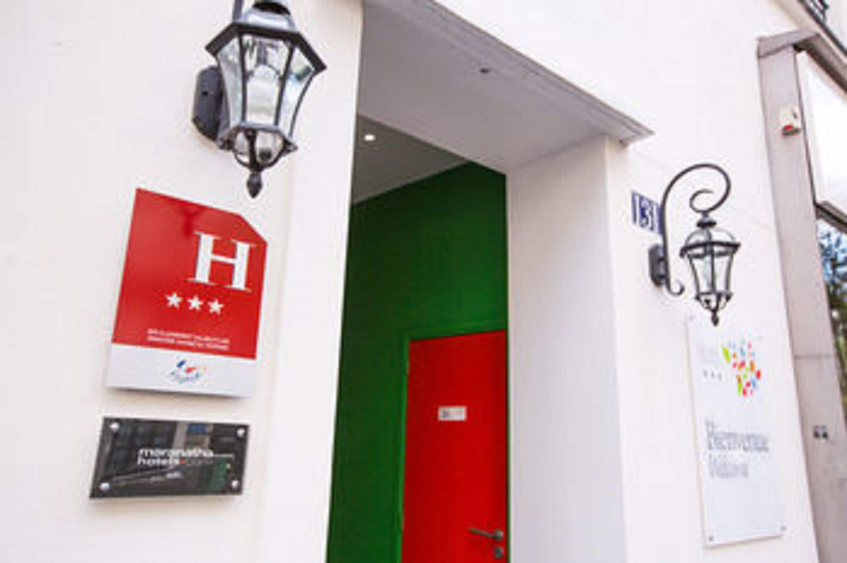 A hotel entrance with a red door, a sign with a white 'H' and three stars, and a sign indicating 'Hotel' and 'Business Center'.